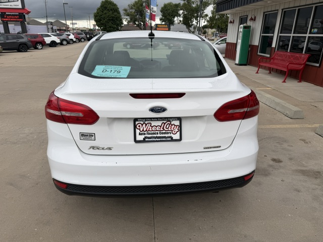 Rear view of a white Ford Focus in a dealership lot, with a Wheel City Auto Finance Centers plate and a blue sale sticker on the rear window.