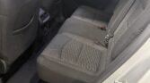 Back seat area of a car with gray cloth seats, visible seat belts, and a center console vent between front seats; door panel on right side and window showing a sign outside.