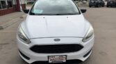 Front view of a white Ford sedan parked in a dealership lot, with a Wheel City license plate frame and a blue sale sticker on the lower-left windshield.