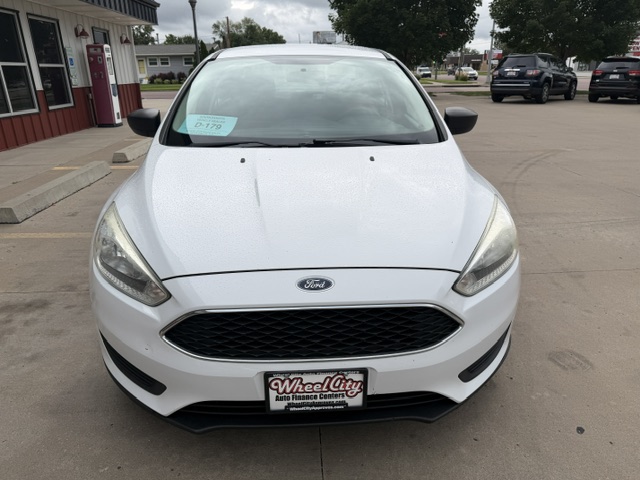 Front view of a white Ford sedan parked in a dealership lot, with a Wheel City license plate frame and a blue sale sticker on the lower-left windshield.