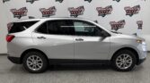 Side view of a silver Chevrolet Equinox SUV indoors with a repeating Wheel City Auto Finance Centers banner in the background.