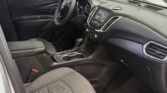 Front interior of a Chevrolet sedan showing the driver seat, steering wheel, center console with touchscreen, and gear shifter in a dark cloth interior.
