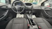Front interior of a compact car showing steering wheel, center console, and front seats from a passenger-side perspective.