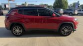 Red Jeep Cherokee SUV parked in a car lot, side view with black roof rails, tinted windows, and silver alloy wheels.