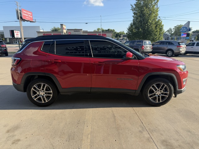 Red Jeep Cherokee SUV parked in a car lot, side view with black roof rails, tinted windows, and silver alloy wheels.