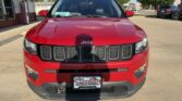 Front view of a red Jeep SUV parked in a dealership lot, featuring the seven-slot grille and a Wheel City license plate.