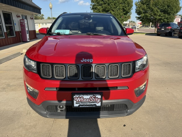 Front view of a red Jeep SUV parked in a dealership lot, featuring the seven-slot grille and a Wheel City license plate.