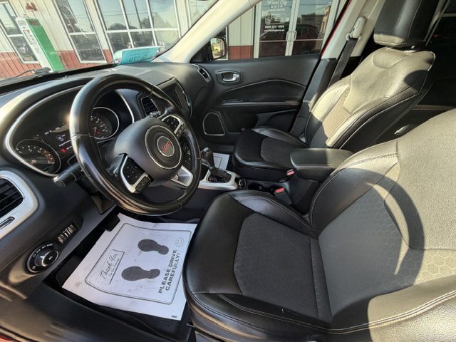 Inside a Jeep SUV with black leather seats, steering wheel with Jeep badge, center console, and a dealership paper on the floor mat.