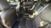 Dark leather back seat of a car with three seating positions and visible seat belts and headrests in a well-lit cabin.