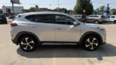 Side view of a silver SUV parked in a car dealership lot with other cars in the background.