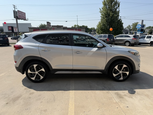 Side view of a silver SUV parked in a car dealership lot with other cars in the background.