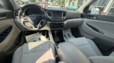 Interior of a light gray Hyundai car viewed from the back seat, showing the steering wheel, dashboard, center console, and front seats bathed in sunlight.