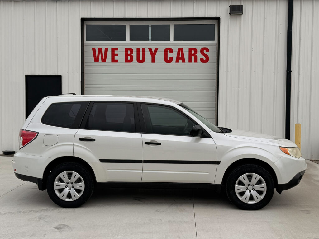 White SUV parked in front of a garage door with a bold red 'WE BUY CARS' sign on it