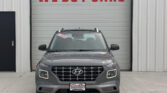 Front view of a gray Hyundai SUV parked in front of a metal building with a red 'WE BUY CARS' sign on the garage door, windshield sticker visible.