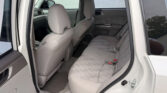 Rear passenger area of a light gray SUV with two rows of fabric seats, rear door open and parking lot outside visible.
