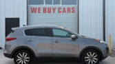 Car dealership with a large 'WE BUY CARS' sign on a garage door; silver SUV in foreground.