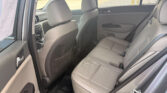 Rear passenger area of a beige car with open door, showing the back seat and front seats; parked cars visible outside a parking lot.