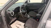 Interior of a gray SUV front cabin with steering wheel, dashboard, center console, and black-stitched seats; paper floor mat visible on driver side