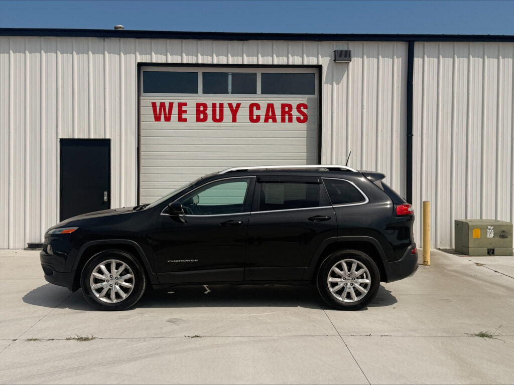 Industrial building with a white garage door that reads 'WE BUY CARS' in red, and a black SUV parked in front.