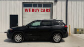 Industrial building with a white garage door that reads 'WE BUY CARS' in red, and a black SUV parked in front.