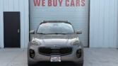 Gray Kia SUV parked in front of a garage door with a large red 'WE BUY CARS' sign above it.
