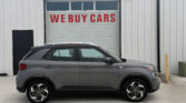 Gray SUV parked in front of a white metal building with a large garage door that says 'WE BUY CARS' in red letters.
