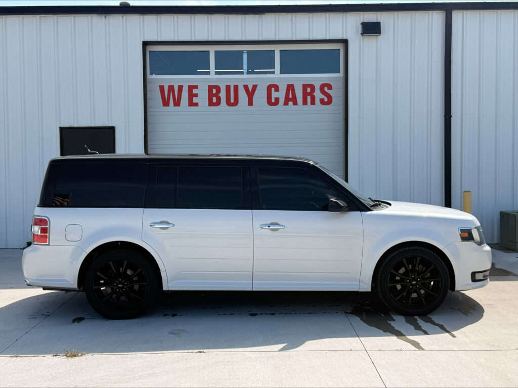 White SUV parked in front of a garage door with a large red 'WE BUY CARS' sign above it.