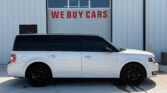 White SUV parked in front of a garage door with a large red 'WE BUY CARS' sign above it.