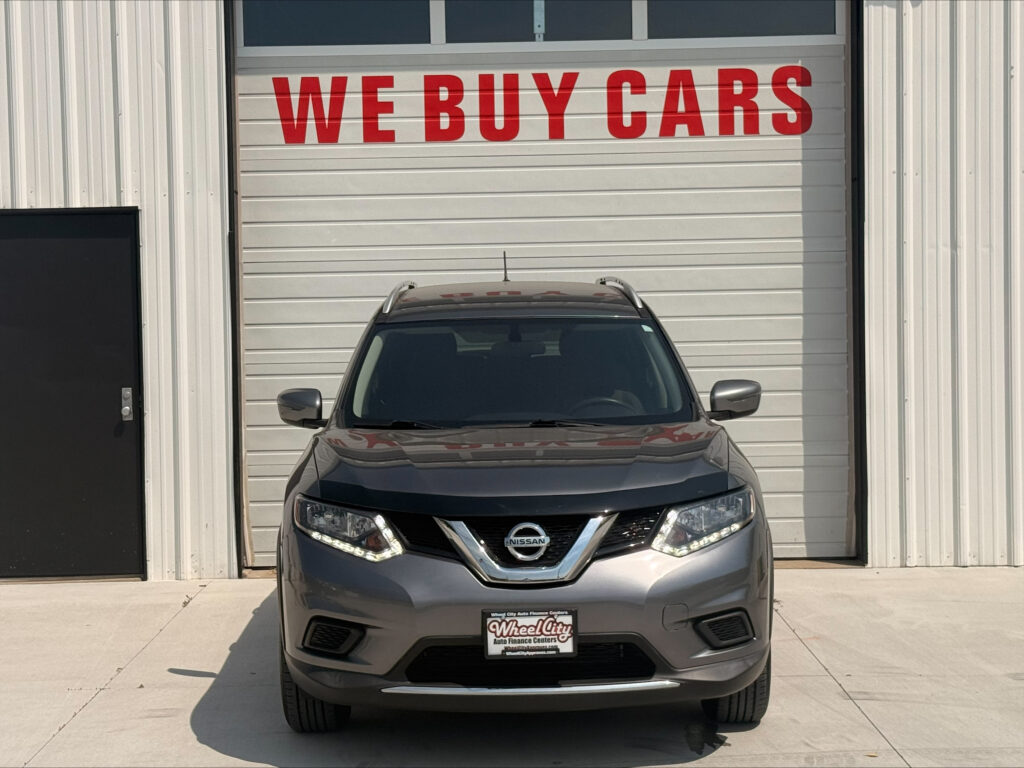 Gray Nissan SUV parked in front of a white garage door with a large red 'WE BUY CARS' sign above.