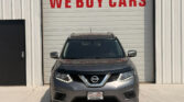 Gray Nissan SUV parked in front of a white garage door with a large red 'WE BUY CARS' sign above.