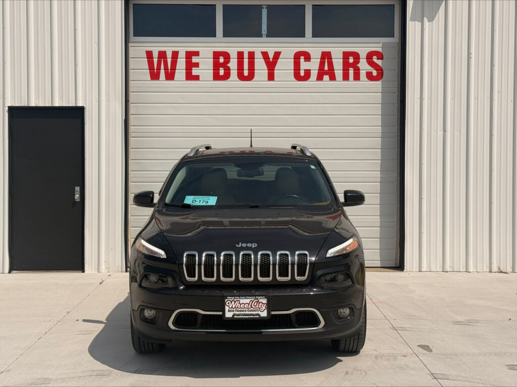 Front view of a black Jeep parked in front of a garage door with a large red 'WE BUY CARS' sign above it.