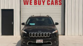 Front view of a black Jeep parked in front of a garage door with a large red 'WE BUY CARS' sign above it.
