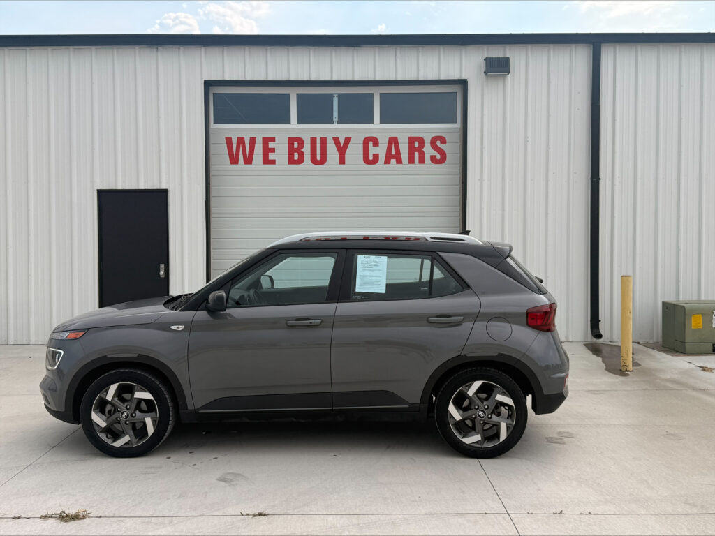 Gray SUV parked in front of a white industrial building with a red 'WE BUY CARS' sign on the garage door