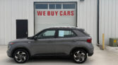 Gray SUV parked in front of a white industrial building with a red 'WE BUY CARS' sign on the garage door