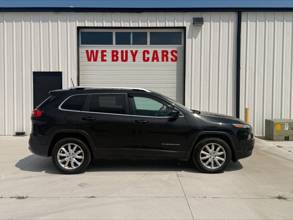 Black Jeep Cherokee SUV parked in front of a white garage door with a red 'WE BUY CARS' sign above it