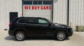 Black Jeep Cherokee SUV parked in front of a white garage door with a red 'WE BUY CARS' sign above it