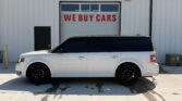 White minivan parked in front of a building with a large 'WE BUY CARS' sign on a garage door in the background.