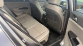 Rear car passenger area with beige leather seats, view of backseat and front seats, open rear door, center console and door panels visible