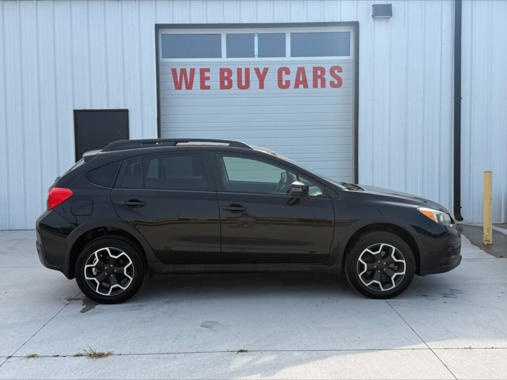 Black SUV parked in front of a blue industrial building with a large 'WE BUY CARS' sign on a garage door.