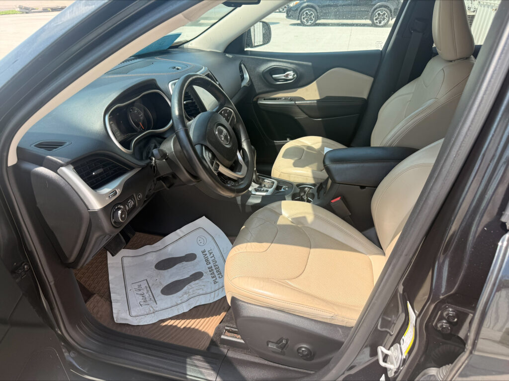 Front interior of a black SUV with beige leather seats, steering wheel, and center console; paper floor mat on the driver’s side in view.