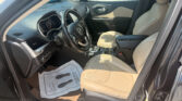 Front interior of a black SUV with beige leather seats, steering wheel, and center console; paper floor mat on the driver’s side in view.