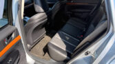 Back seat area of a car with black leather seats and wood-accent door panel visible through an open rear door into a sunlit exterior.