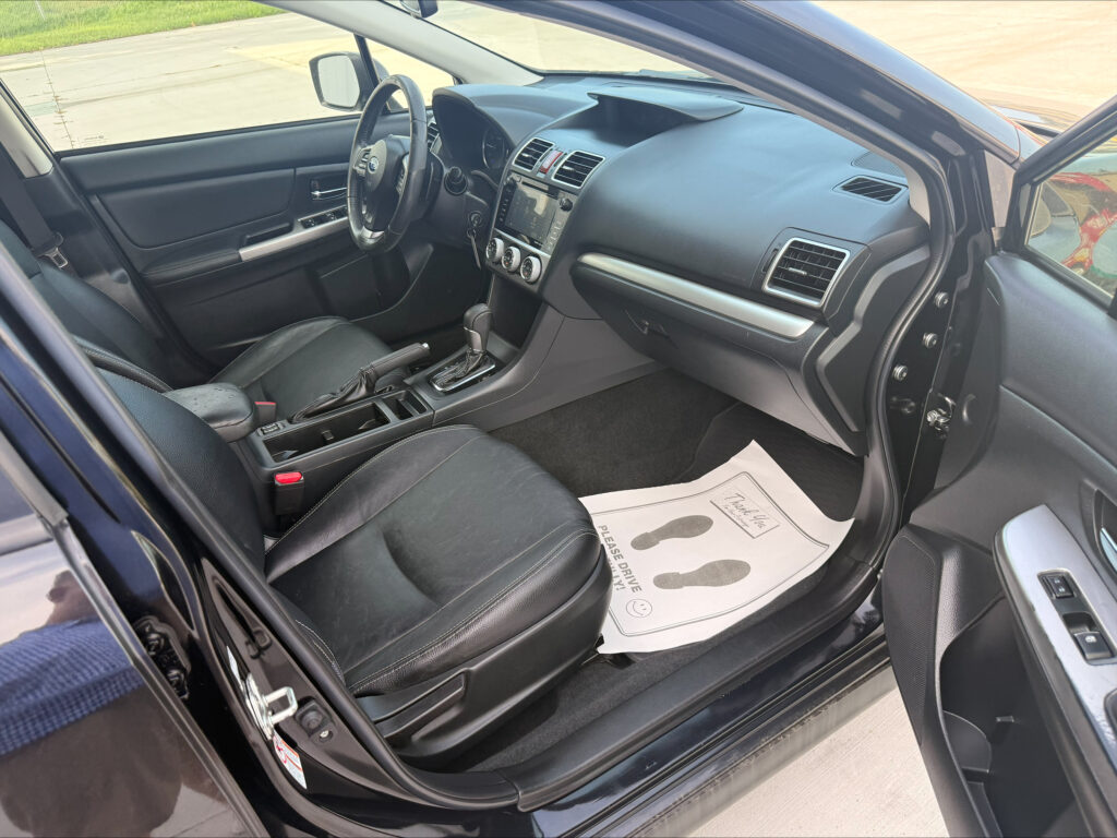 Interior of a dark SUV showing the driver’s seat, steering wheel, center console with a touchscreen, and the open front passenger area; door is open.
