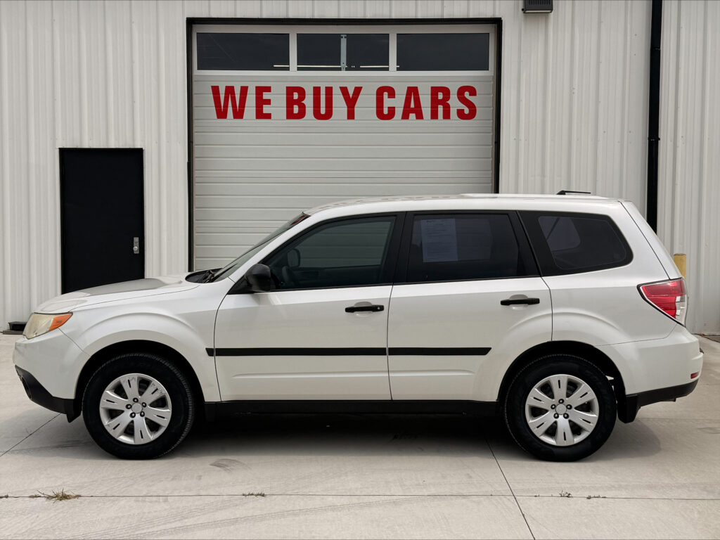 White SUV parked in front of a warehouse with a large garage door reading 'WE BUY CARS' in red letters