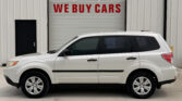 White SUV parked in front of a warehouse with a large garage door reading 'WE BUY CARS' in red letters