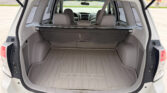Open rear hatch of a white Subaru SUV showing the gray cargo area with a folded tonneau cover and the back of the rear seats visible.