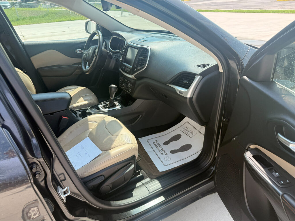 Open front driver’s door of a black SUV, view of beige leather seats and center console.