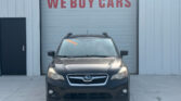 Front view of a dark gray Subaru SUV parked in front of a large light-gray garage door with a red 'WE BUY CARS' sign above the door.