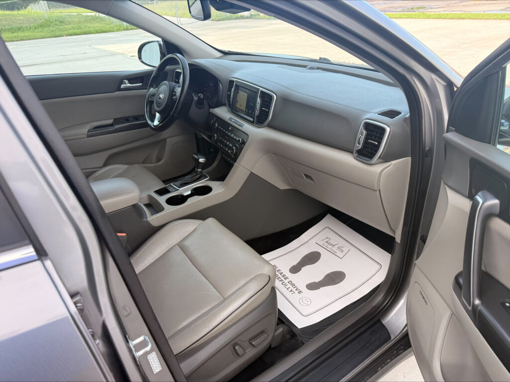 Interior view of a modern SUV cabin with front seats, steering wheel, center touchscreen, and gear shifter, driver-side door open