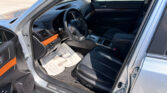 Open driver's door view of a Subaru interior, showing the steering wheel, dashboard, center console, and a paper floor mat on the driver’s side